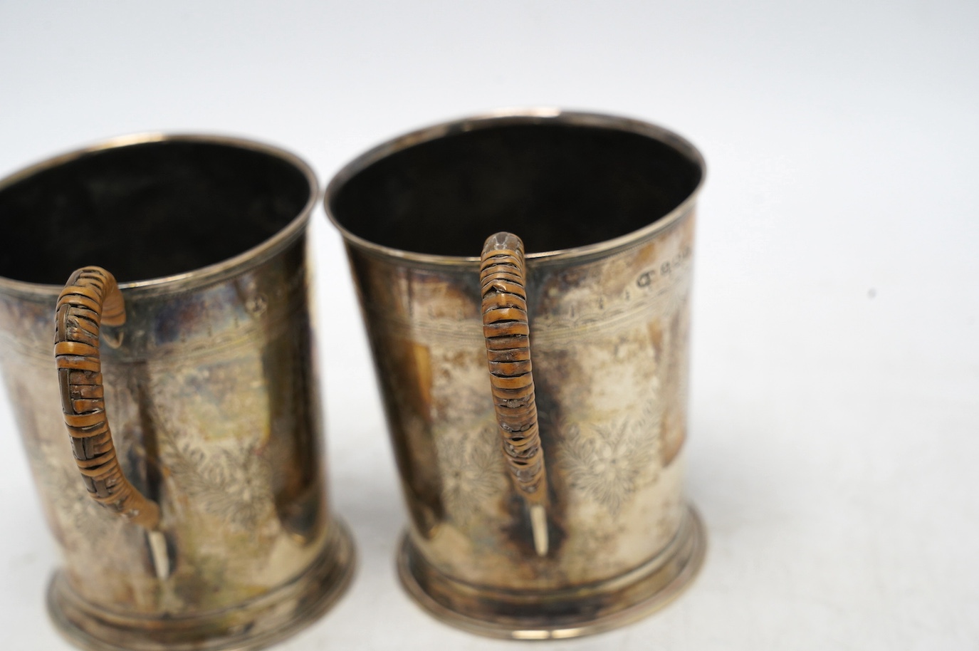 A pair of George V engraved silver mugs, with rattan handles, William Aitken, Birmingham, 1920, height 95mm, gross weight 5.9oz. Condition - fair